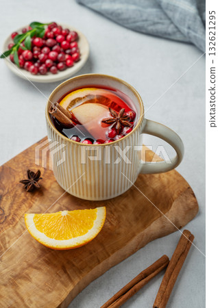 A hot cranberry Christmas drink in a mug on a wooden board on a light background with cinnamon 132621295