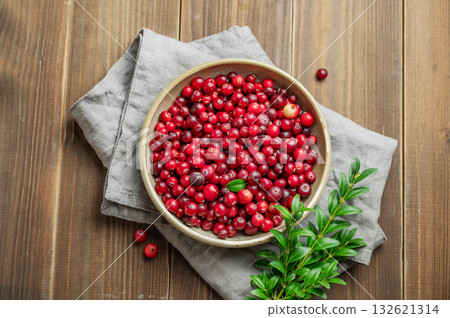 Fresh cranberries in a dark bowl on a wooden background with green branch and napkin. Fresh cranberries in a dark bowl on a wooden background with green branch and napkin. 132621314