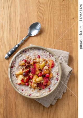 Overnight oatmeal with apple, cranberry and cinnamon in a plate on a wooden background with spoon  132621320