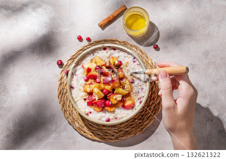 Hand holding spoon in to plate of oatmeal with apple, cranberry and cinnamon on a light background 132621322