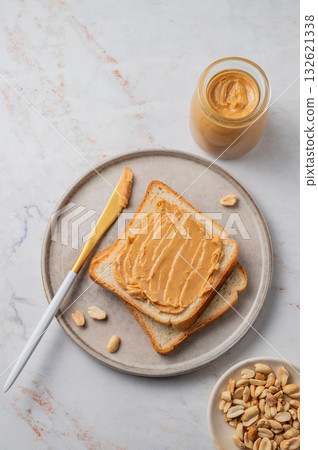 Peanut butter toast on a plate on a light marble background with nuts and knife. Peanut butter toast on a plate on a light marble background with nuts and knife. 132621338