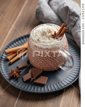 Hot chocolate in a cup with whipped cream and spices on a dark plate on a rustic wooden background. 132621358