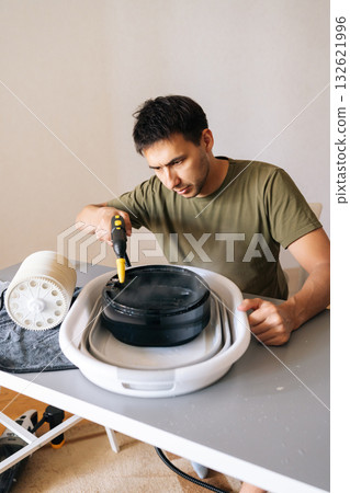 Vertical shot of focused man meticulously cleaning filter of air humidifier with steam cleaner, promoting optimal performance and maintaining high standards of hygiene for indoor air quality. 132621996