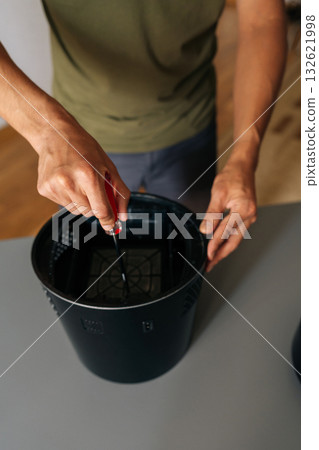 Technician male repairing air humidifier, focusing on precision work and professional maintenance of home electronic device, close-up. Concept of hygiene and cleanliness in domestic environment. Technician male repairing air humidifier, focusing on precision work and professional maintenance of home electronic device, close-up. Concept of hygiene and cleanliness in domestic environment. 132621998