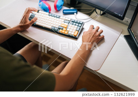 Close-up of unrecognizable remote programmer focusing on coding project, utilizing dual-screen workspace with mechanical keyboard, seated in ergonomic gaming chair. Concept of remote workplace. 132621999