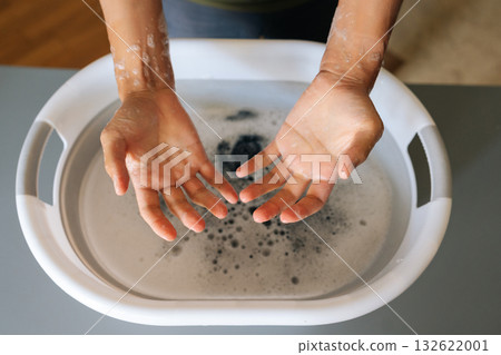Top view of housekeeper showing clean hands after washing clothes in basin filled with soapy water, demonstrating effectiveness of handwashing in maintaining hygiene after household chores, close-up. Top view of housekeeper showing clean hands after washing clothes in basin filled with soapy water, demonstrating effectiveness of handwashing in maintaining hygiene after household chores, close-up. 132622001