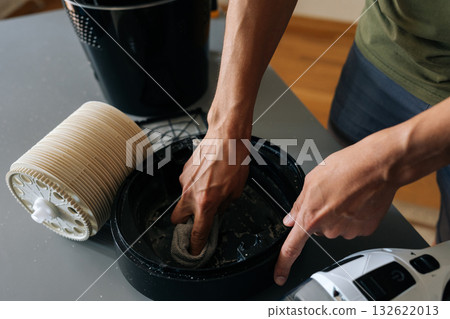 Skilled technician wiping interior components of air humidifier, vacuum cleaner positioned nearby for thorough dust removal and maintenance. Concept of maintenance modern home appliance. Skilled technician wiping interior components of air humidifier, vacuum cleaner positioned nearby for thorough dust removal and maintenance. Concept of maintenance modern home appliance. 132622013