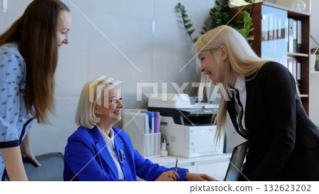 Three joyful businesswomen share a light hearted moment in a contemporary office, laughing and commemorating their successes Three joyful businesswomen share a light hearted moment in a contemporary office, laughing and commemorating their successes 132623202
