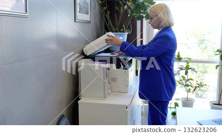 Efficiently managing daily tasks, businesswoman in blue suit using a multifunction printer in a modern office with large windows and plants Efficiently managing daily tasks, businesswoman in blue suit using a multifunction printer in a modern office with large windows and plants 132623206