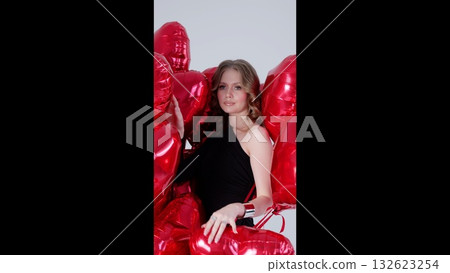 Elegant woman standing amidst bright red heart shaped balloons, radiating romantic mood and celebration spirit for valentine's day or special event 132623254