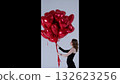 Young woman grasping red heart shaped balloons, embodying romantic celebration with graceful smile, standing against crisp white studio backdrop, expressing festive valentine's mood 132623256