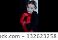 Stylish woman posing in red satin gloves, matching tights, sophisticated black jacket, creating dramatic contrast against shadowy studio backdrop 132623258