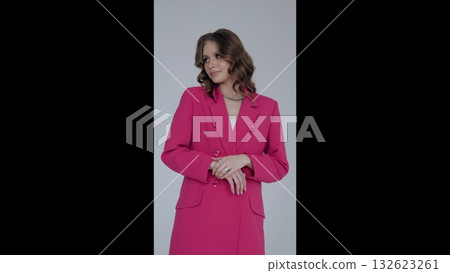 Professional businesswoman wearing tailored pink suit and silver necklace, standing confidently in studio, hand resting delicately, gazing off camera against soft gray backdrop Professional businesswoman wearing tailored pink suit and silver necklace, standing confidently in studio, hand resting delicately, gazing off camera against soft gray backdrop 132623261