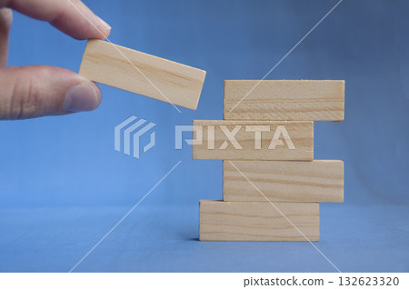 Hand preparing to place wooden block on lower stack showing teamwork and foundation concept with customizable space for text or ideas. Hand preparing to place wooden block on lower stack showing teamwork and foundation concept with customizable space for text or ideas. 132623320