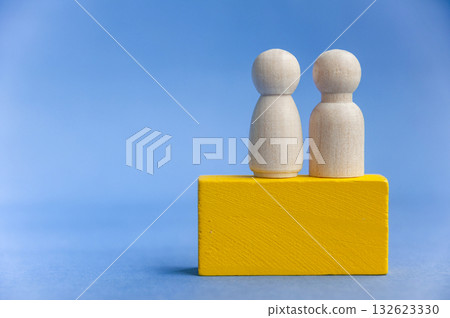 Two wooden peg figures on yellow block with blue background symbolizing teamwork. With customizable space for text or ideas 132623330