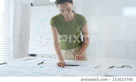 Businesswoman pointing at financial charts and graphs on a table, with a pie chart on a flip chart in the background. Business people concept Businesswoman pointing at financial charts and graphs on a table, with a pie chart on a flip chart in the background. Business people concept 132623790