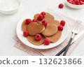 A heap of heart shaped pancakes on the white plate with raspberries on the white background 132623866
