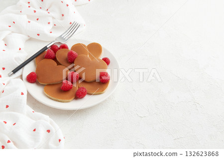 A heap of heart shaped pancakes with raspberries and a fork on the white plate on white background A heap of heart shaped pancakes with raspberries and a fork on the white plate on white background 132623868