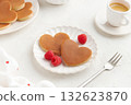 Two heart shaped pancakes with raspberries and a fork on the white plate on white background 132623870