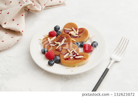 A heap of heart shaped pancakes with berries and a fork on the white plate on grey background A heap of heart shaped pancakes with berries and a fork on the white plate on grey background 132623872