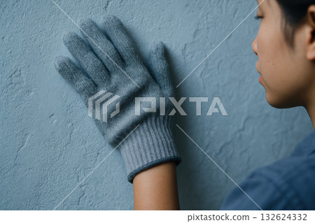 Person wearing gray wool glove touching textured blue wall with hand, highlighting sense of touch and tactile perception indoors, AI Generative 132624332