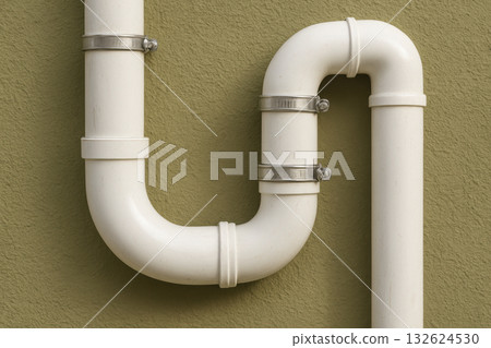 White pvc drainage pipes mounted on an exterior green wall with metal clamps forming a u shaped bend for plumbing system maintenance, AI Generative White pvc drainage pipes mounted on an exterior green wall with metal clamps forming a u shaped bend for plumbing system maintenance, AI Generative 132624530