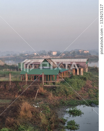 A wide shot of a large, modern building with a green roof, surrounded by lush vegetation and water, under a hazy sky A wide shot of a large, modern building with a green roof, surrounded by lush vegetation and water, under a hazy sky 132625127