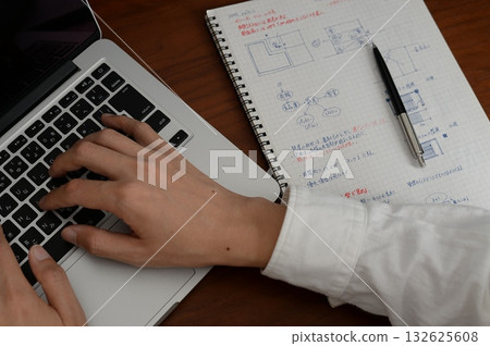 桌上放著筆記型電腦，建築師的手正在筆記本上寫設計筆記。 132625608