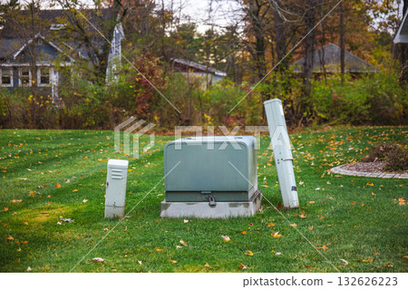 Utility boxes on a residential lawn surrounded by autumn foliage and houses in the background during fall season. 132626223