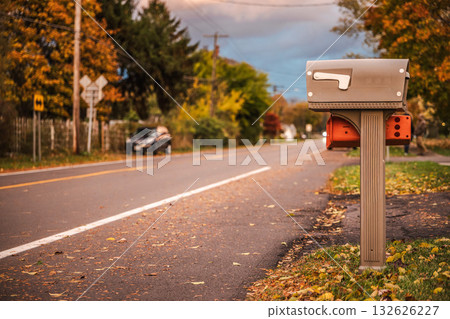 Mailbox on a quiet suburban road in the USA during autumn, surrounded by colorful trees and fallen leaves in warm evening light. 132626227