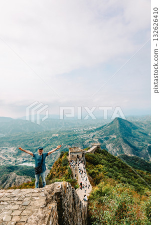 Happy man on Simatai section of Great Wall of China in its original, un-restored state. Watchtowers perched on mountain peaks, China, Beijing. Vertical photo Happy man on Simatai section of Great Wall of China in its original, un-restored state. Watchtowers perched on mountain peaks, China, Beijing. Vertical photo 132626410