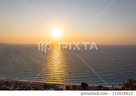 Panoramic view of Mediterranean Sea from sandy beach with rays of sun against backdrop of colorful sunset of Rhodes, Greece. Vacation, holiday concept. High quality photo 132626622
