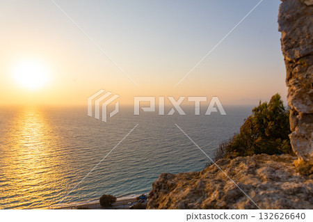 Panoramic view of Mediterranean Sea from sandy beach with rays of sun against backdrop of colorful sunset of Rhodes, Greece. Vacation, holiday concept. High quality photo 132626640
