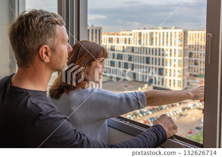 Man hugging his wife. Young couple moving in new apartmen. People looks out window at new houses. Concept new homes, new beginning. High quality photo Man hugging his wife. Young couple moving in new apartmen. People looks out window at new houses. Concept new homes, new beginning. High quality photo 132626714