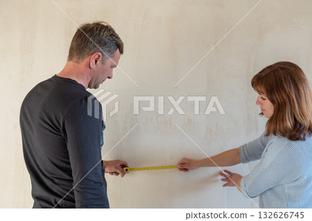 Young couple moving in new apartmen. People measure size of wall with tape measure. Concept new homes, new beginning. High quality photo Young couple moving in new apartmen. People measure size of wall with tape measure. Concept new homes, new beginning. High quality photo 132626745