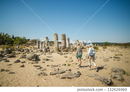 Two women explore the ancient limestone pillars of Pobiti Kamani, also known as the Stone Desert, near Varna, Bulgaria, under a bright blue summer sky. 132626960