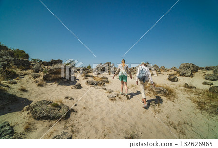 Two women hiking through the sandy and rocky landscape of Pobiti Kamani in Bulgaria under a clear blue summer sky. Two women hiking through the sandy and rocky landscape of Pobiti Kamani in Bulgaria under a clear blue summer sky. 132626965