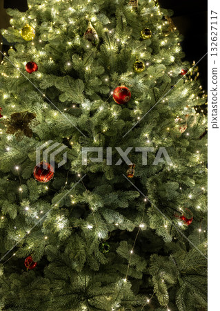 Close-up of a glowing Christmas tree decorated with red and gold ornaments and warm lights, creating a festive and cozy holiday atmosphere. Close-up of a glowing Christmas tree decorated with red and gold ornaments and warm lights, creating a festive and cozy holiday atmosphere. 132627117