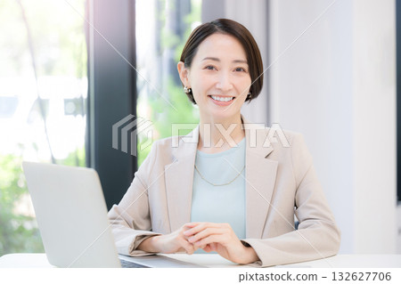 A businesswoman working on a computer by a window with greenery, looking at the camera 132627706