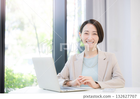 A businesswoman working on a computer by a window with greenery, looking at the camera 132627707