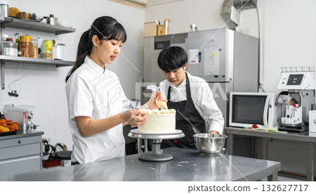 A woman working part-time at a cake shop squeezes fresh cream onto a cake and decorates it 132627717