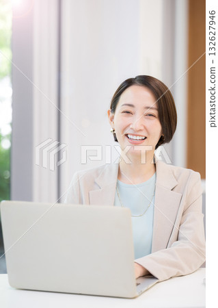 A businesswoman working on a computer by a window with greenery, looking at the camera A businesswoman working on a computer by a window with greenery, looking at the camera 132627946