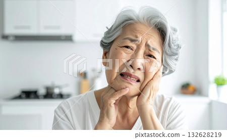 Elderly woman resting her chin on her hands at the kitchen table 132628219