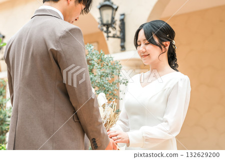 新郎新娘手捧花束，面對面站著（婚禮，新娘，情侶） 132629200