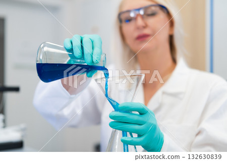 Woman scientist using a glass funnel to pour liquid solution in a laboratory. Represents accuracy, research, chemistry, and modern scientific techniques in laboratory work. Woman scientist using a glass funnel to pour liquid solution in a laboratory. Represents accuracy, research, chemistry, and modern scientific techniques in laboratory work. 132630839