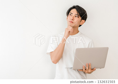 A young Asian man holding a laptop and worrying, thinking, and considering A young Asian man holding a laptop and worrying, thinking, and considering 132631503