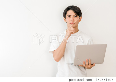 A young Asian man holding a laptop and worrying, thinking, and considering A young Asian man holding a laptop and worrying, thinking, and considering 132631507