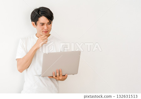 A young Asian man holding a laptop and thinking (trouble, failure, mistake) 132631513