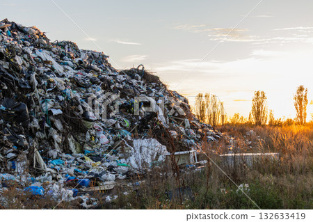 A vast landfill filled with garbage and rubbish is seen as the sun sets in the background, casting warm light over the polluted area A vast landfill filled with garbage and rubbish is seen as the sun sets in the background, casting warm light over the polluted area 132633419