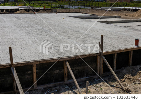 Construction site showing a newly poured concrete slab, ready for building a house, surrounded by a developing neighborhood in daylight Construction site showing a newly poured concrete slab, ready for building a house, surrounded by a developing neighborhood in daylight 132633446